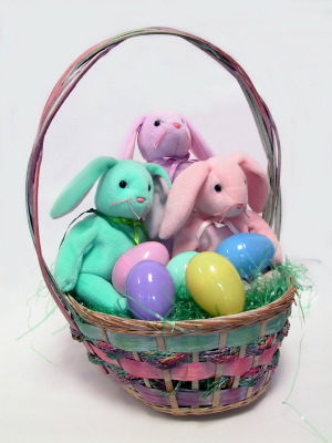 Three stuffed bunny rabbits in an easter basket with colorful eggs in pastel colors.