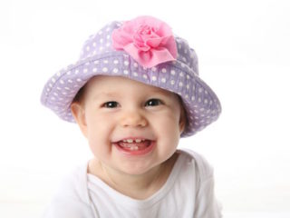 8046087_l 8046087 - smiling baby girl showing teeth wearing a purple polka dot hat with pink flower isolated on white background