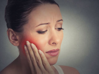 41484635_l 41484635 - closeup portrait young woman with sensitive tooth ache crown problem about to cry from pain touching outside mouth with hand isolated grey wall background. negative emotion facial expression feeling